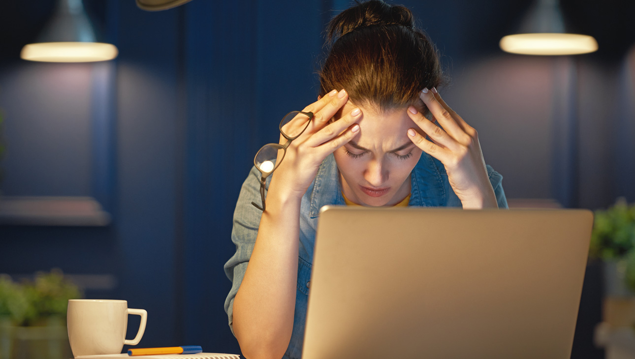 Woman Clutching Head In Front Of Laptop.