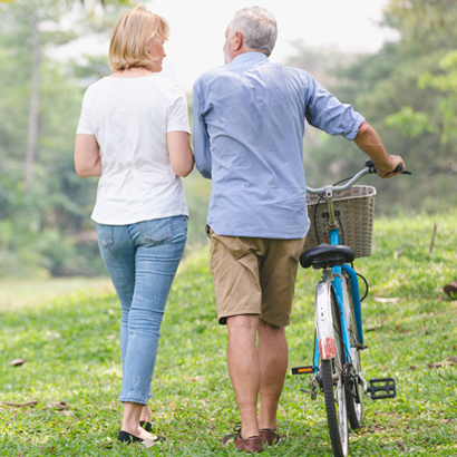 Man and Woman Pushing Bicycle Through Field.