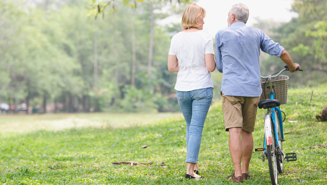 Man Pushing Bicycle While Walking With Woman Across A Field.