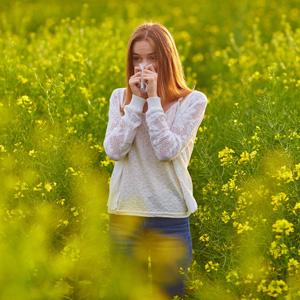 Woman Blowing Nose In Field Of Flowers.