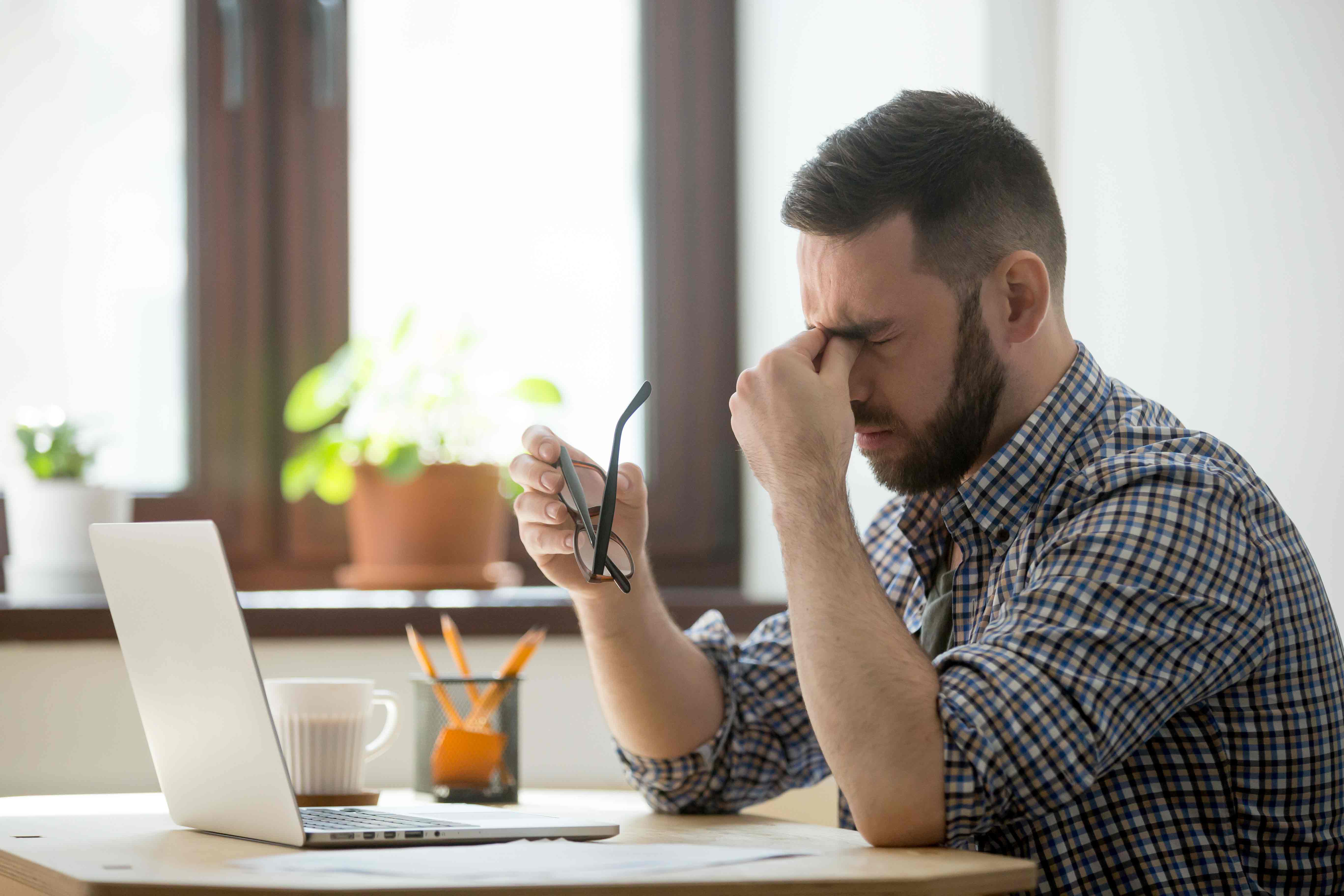 Man Squeezing Tired Eyes In Front Of Laptop.